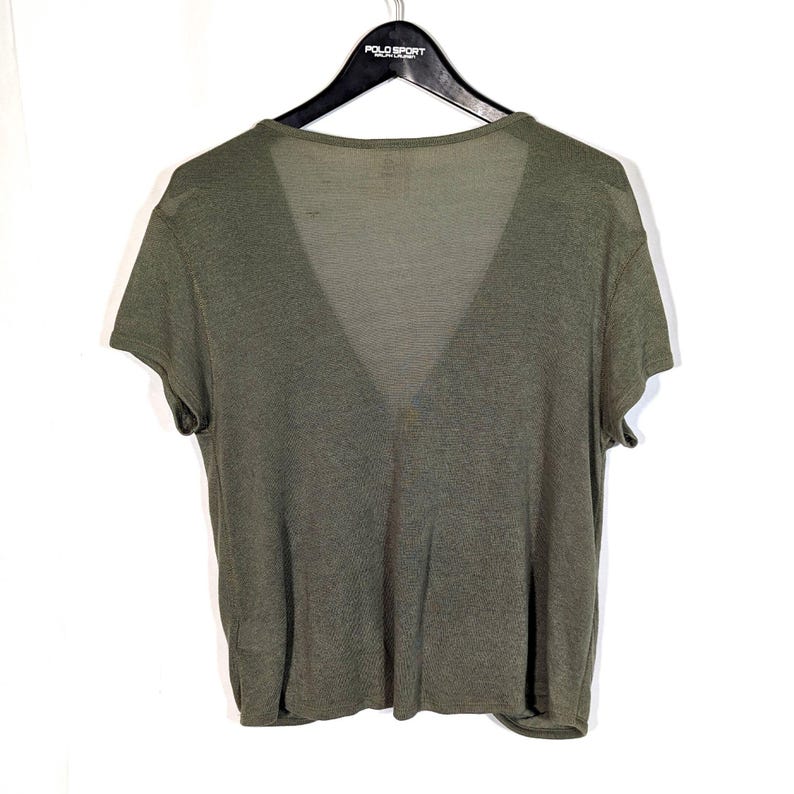 May include: Olive green V-neck short-sleeve shirt hanging on a black hanger. The shirt is made of a lightweight, semi-sheer fabric. The Polo Sport logo is visible on the hanger.