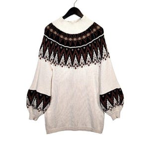 Puede incluir: Su&eacute;ter color crema con cuello alto y mangas largas. La parte superior del pecho y las mangas presentan un estampado geom&eacute;trico en marr&oacute;n y negro. El su&eacute;ter est&aacute; colgado de una percha negra sobre un fondo blanco.