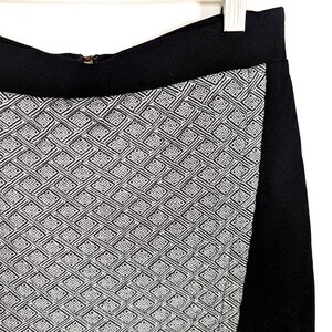 May include: A black skirt with a geometric pattern in white and black. The skirt has a wide black waistband and a side panel of solid black fabric. The geometric pattern is a repeating design of interlocking shapes.