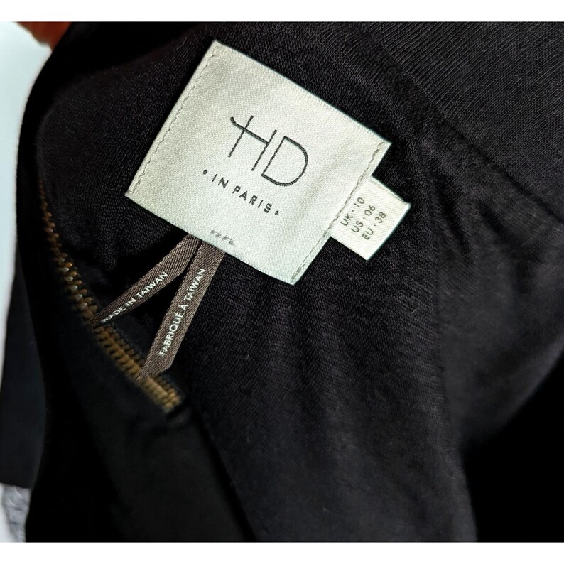 May include: Close-up of a black garment with a zipper and tags. The tags read "HD IN PARIS", "MADE IN TAIWAN", and size information: UK 10, US 06, EU 38. The zipper is a gold color.