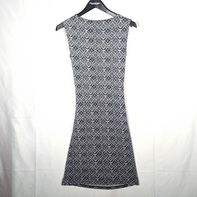 Puede incluir: Vestido sin mangas con un estampado geom&eacute;trico en tonos grises y azul marino. El vestido est&aacute; colgado de una percha negra. El estampado consiste en c&iacute;rculos y rombos entrelazados.