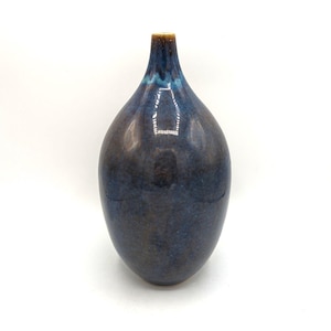 Może przedstawiać: Wazon ceramiczny w ciemnoniebieskim kolorze, o zaokrąglonym korpusie i wąskiej szyjce. Wazon ma nakrapianą glazurę z brązowymi akcentami.