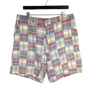 May include: Multi-colored plaid shorts with a patchwork design. The shorts feature a combination of blue, pink, and yellow squares. The shorts are hanging on a black hanger.