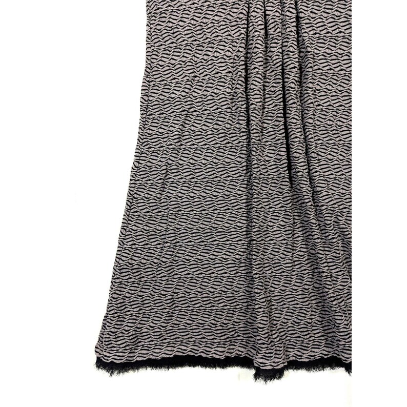May include: A draped fabric with a wave-like pattern in black and gray. The bottom edge has a black fringe. The fabric appears to be a skirt or a piece of clothing.