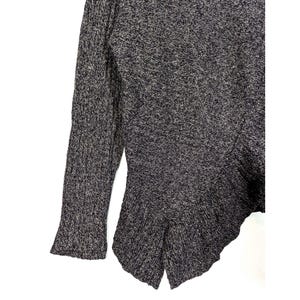 K&ouml;nnte beinhalten: Ein dunkelgrau-wei&szlig; gesprenkelter Strickpullover mit einem ausgestellten, asymmetrischen Saum. Der lange &Auml;rmel hat eine ausgestellte Manschette. Der Pullover ist aus einem strukturierten Strickstoff gefertigt.