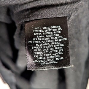 May include: A close-up of a black fabric tag with white text. The tag lists the materials of a garment, including rayon, polyester, spandex, cotton, and modal. The tag also includes the word "shell" and "lining".