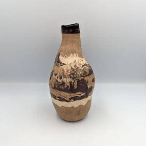 Könnte beinhalten: Eine handgefertigte Keramikvase mit einer einzigartigen, organischen Form. Die Vase hat einen dunkelbraunen Rand und einen Körper mit einem marmorierten Muster aus Beige-, Braun- und Cremetönen. Die Vase ist etwa 20 cm hoch.