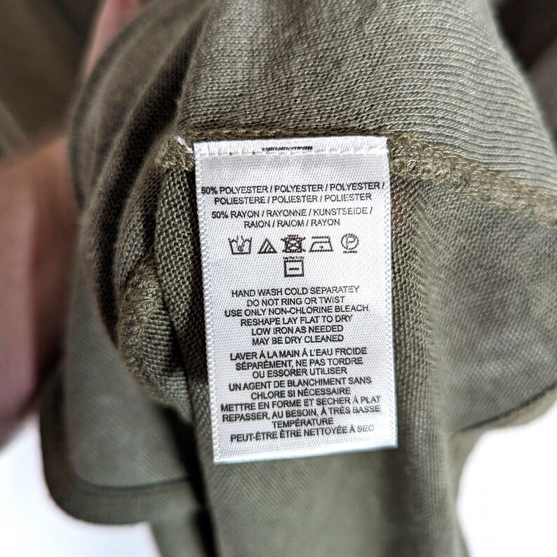 May include: Close-up of a green garment label with care instructions. The label includes text detailing washing, drying, and ironing instructions. The fabric composition is listed as 50% polyester and 50% rayon.