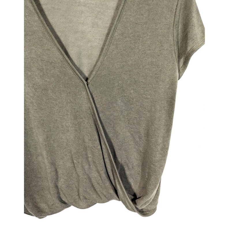 May include: A sage green wrap-style top with a V-neckline and short sleeves. The fabric appears to be a soft knit material. The top has a draped design that gathers at the waist.