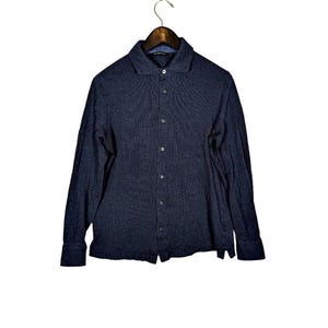 May include: A navy blue long-sleeve button-down shirt with a collared neckline. The shirt is made of a textured fabric and hangs on a wooden hanger against a white background. The shirt has a classic, casual style.