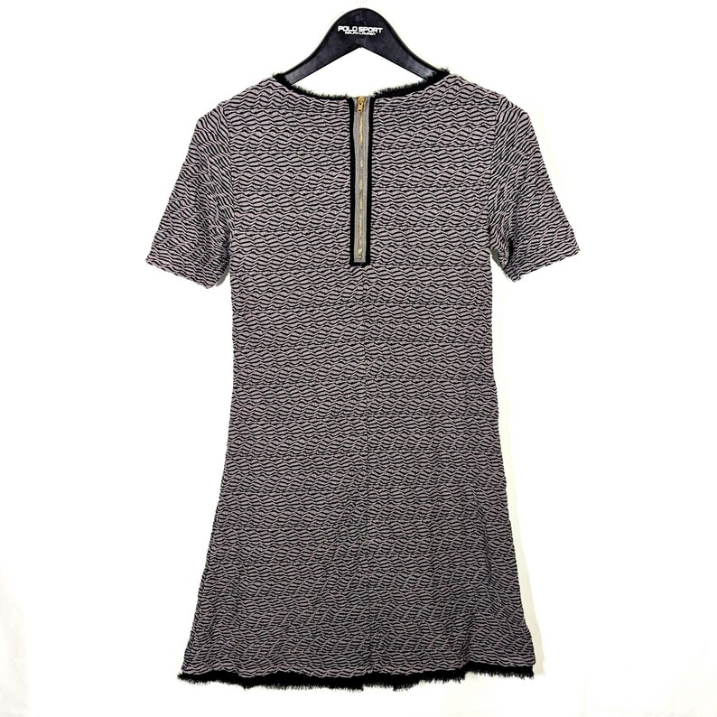 May include: A short-sleeved dress with a textured pattern in shades of gray and black. The dress features a gold zipper down the back and a black fringe at the hemline. The neckline is trimmed with black fabric.
