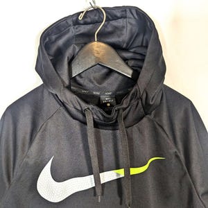 May include: Black Nike Dri-FIT hoodie with a drawstring hood. The Nike swoosh logo is on the front, with a white and neon green design. The hoodie is hanging on a wooden hanger.