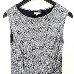Puede incluir: Vestido sin mangas con un estampado geom&eacute;trico en azul marino y blanco. El vestido tiene un cuello redondo y un corpi&ntilde;o ajustado. La etiqueta de la marca "KUT from the Kloth" es visible en el escote. El vestido est&aacute; colgado en una percha negra.