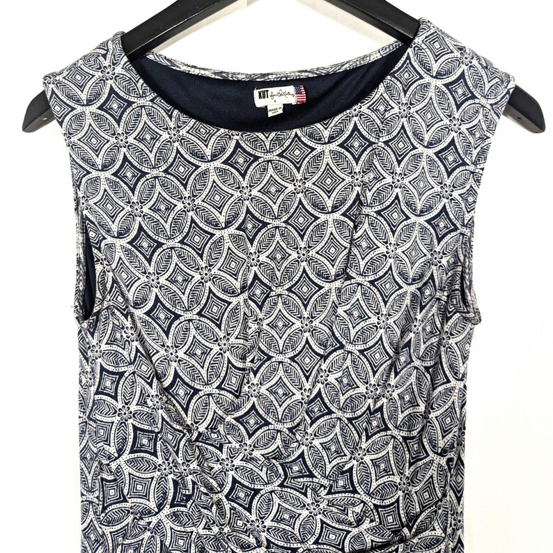 Puede incluir: Vestido sin mangas con un estampado geom&eacute;trico en azul marino y blanco. El vestido tiene un cuello redondo y un corpi&ntilde;o ajustado. La etiqueta de la marca "KUT from the Kloth" es visible en el escote. El vestido est&aacute; colgado en una percha negra.