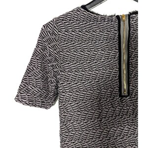 May include: A short-sleeved top with a textured wave pattern in black and light gray. The top features a gold zipper down the back and a black trim around the neckline.