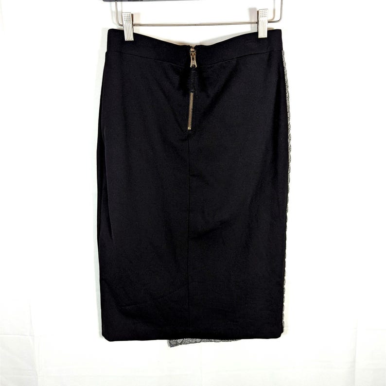 May include: A black pencil skirt with a gold zipper closure at the back. The skirt has a fitted silhouette and a lace detail on the side. The skirt is hanging on a metal hanger against a white background.