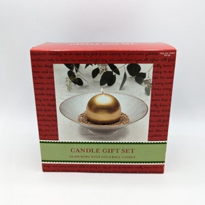 May include: A candle gift set with a gold ball candle in a clear glass bowl. The box features a red and green design with the text "Candle Gift Set" and "Glass Bowl with Gold Ball Candle".
