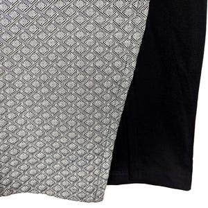 May include: A section of a garment featuring a geometric pattern in shades of gray and white, contrasted by a solid black fabric. The patterned section has a woven appearance, creating a textured look.