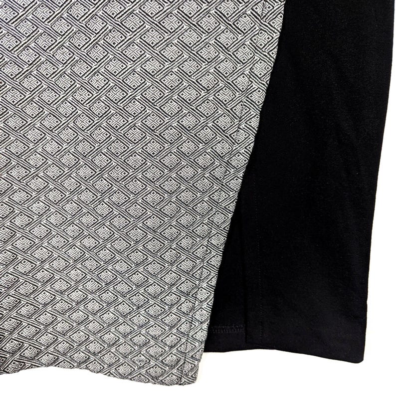 May include: A section of a garment featuring a geometric pattern in shades of gray and white, contrasted by a solid black fabric. The patterned section has a woven appearance, creating a textured look.