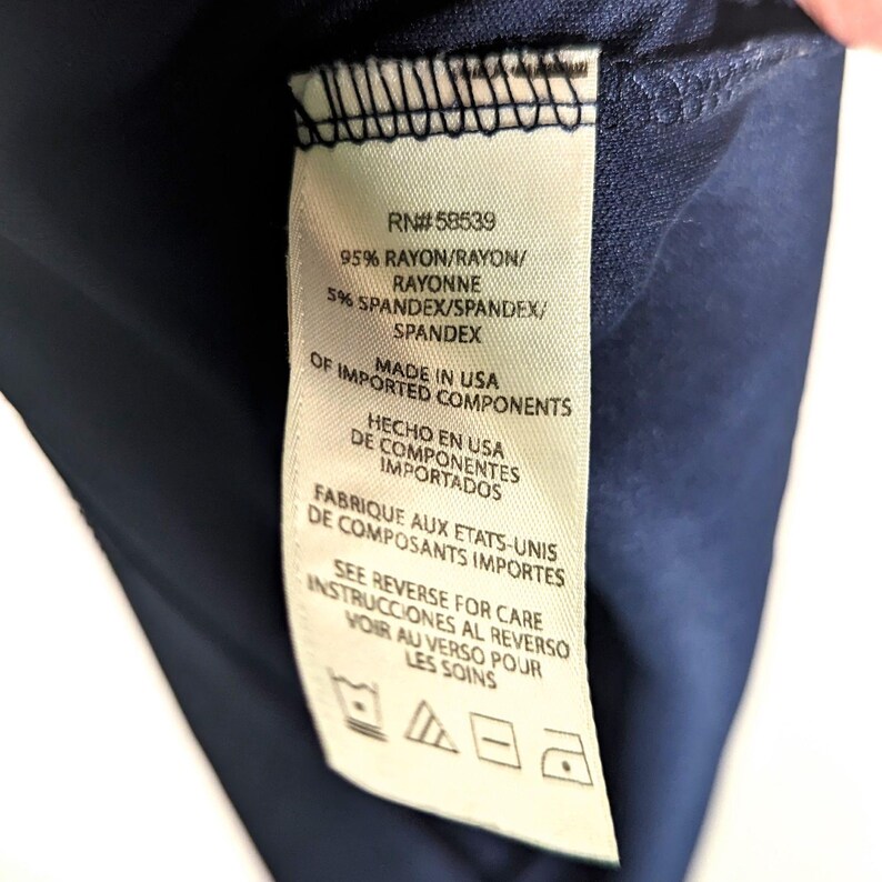 Puede incluir: Primer plano de una tela azul marino con una etiqueta blanca. La etiqueta indica la composici&oacute;n de la tela: 95% ray&oacute;n y 5% spandex. Tambi&eacute;n indica "Made in USA of Imported Components."