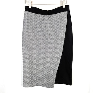 May include: A black and white patterned pencil skirt with a black waistband and a side slit. The skirt is hanging on a white hanger against a white background. The skirt's pattern is a repeating geometric design.