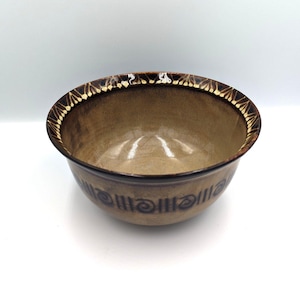 May include: A brown ceramic bowl with a white and brown geometric design around the rim. The bowl has a smooth, glazed interior.