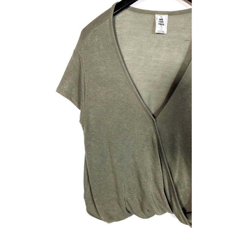 May include: Olive green short-sleeve wrap top with a deep V-neck. The top has a draped design and is made of a soft, lightweight fabric. A tag with the text "WE THE FREE" is visible near the neckline. The top is hanging on a black hanger.