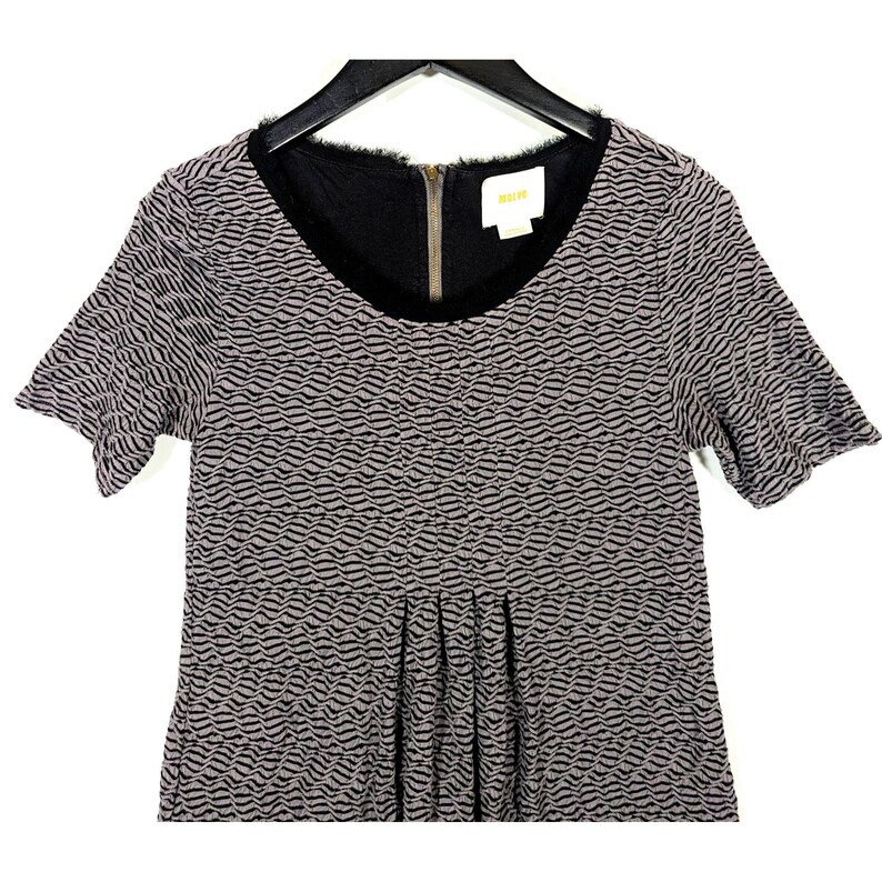 May include: A short-sleeved dress with a textured wave pattern in gray and black. The dress features a black neckline with a gold zipper and a small label. The garment is hanging on a black hanger.