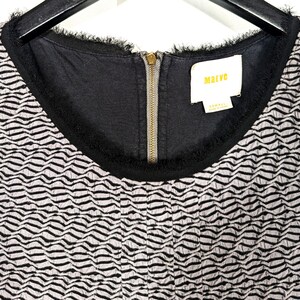 May include: Close-up of a black and white patterned dress. The dress has a black neckline with fringe detailing and a gold zipper. The tag reads "Maeve" and "XS/SMALL".