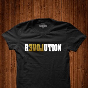 May include: Black t-shirt with the word "REVOLUTION" printed in white letters with a gold outline.