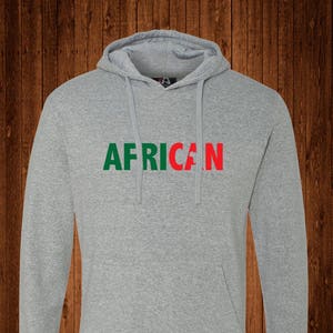 May include: A gray hooded sweatshirt with the word "AFRICAN" printed across the chest. The word "AFRICAN" is in green and red block letters. The sweatshirt has a front pocket and drawstrings.