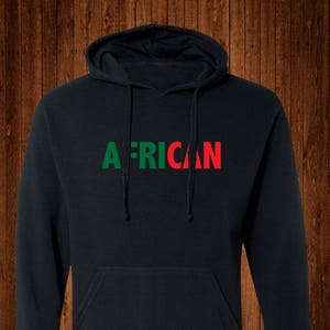 May include: Black hooded sweatshirt with the word "AFRICAN" printed across the chest. The word "AFRICAN" is in green and red block letters. The sweatshirt has a front pocket and a drawstring hood.