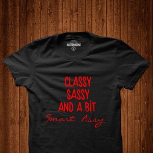 Puede incluir: Camiseta negra con el texto "Classy Sassy And A Bit Smart Assy" en rojo.