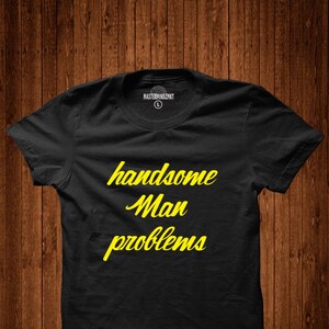 May include: Black t-shirt with yellow text that reads "handsome man problems".