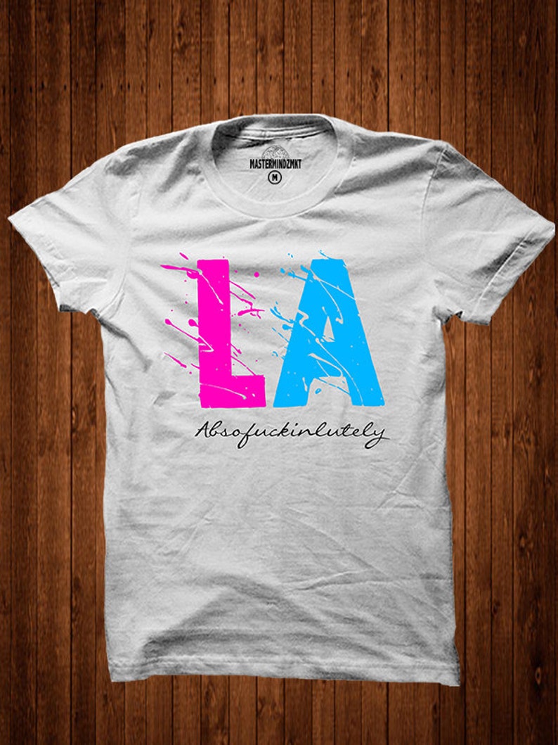 May include: White t-shirt with a pink and blue graphic of the letters "LA" with paint splatters and the text "Absofuckinlutely" underneath.