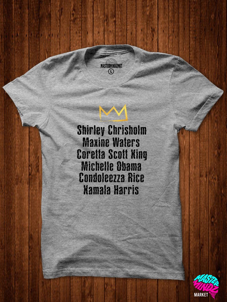 May include: Grey t-shirt featuring a gold crown and a list of names: Shirley Chrisholm, Maxine Waters, Coretta Scott King, Michelle Obama, Condoleezza Rice, Kamala Harris.