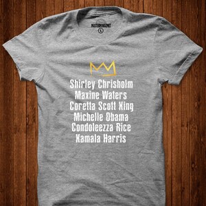 May include: Grey t-shirt with a gold crown and the names Shirley Chrisholm, Maxine Waters, Coretta Scott King, Michelle Obama, Condoleezza Rice, and Kamala Harris printed on it.