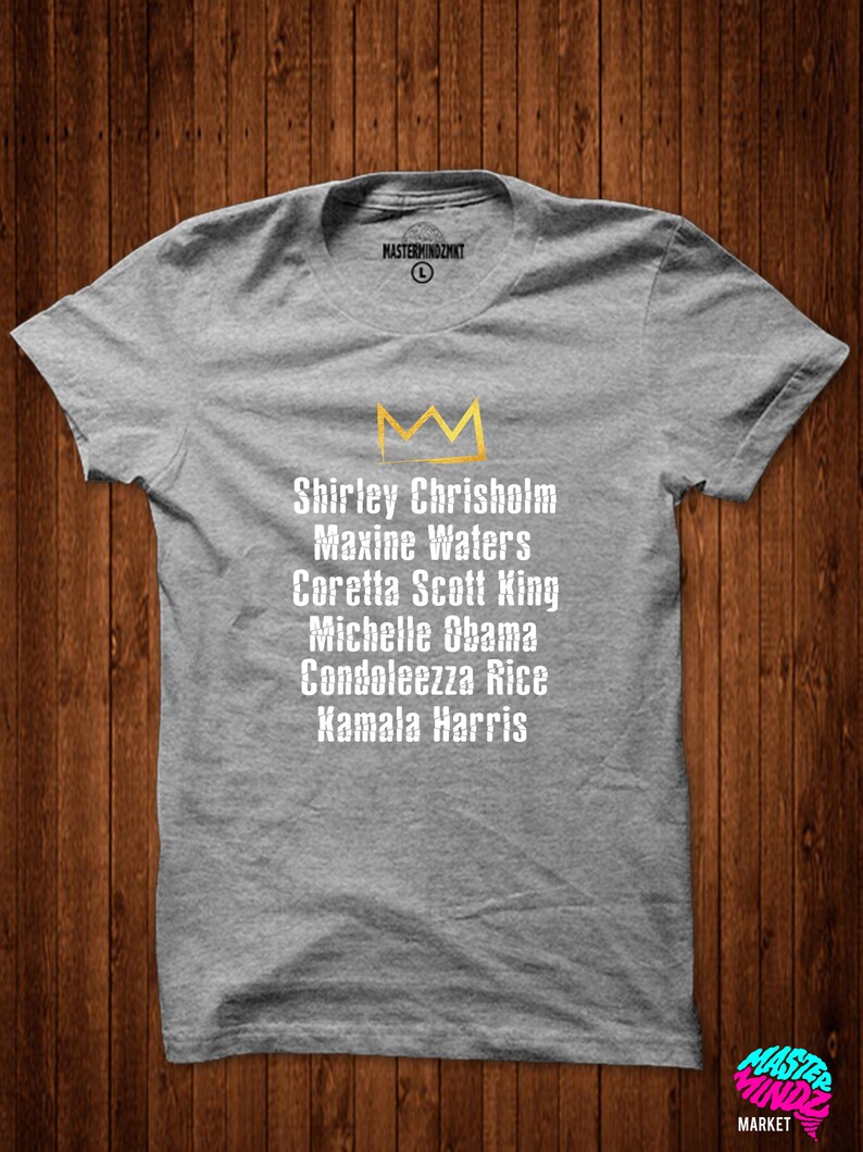 May include: Grey t-shirt with a gold crown and the names Shirley Chrisholm, Maxine Waters, Coretta Scott King, Michelle Obama, Condoleezza Rice, and Kamala Harris printed on it.