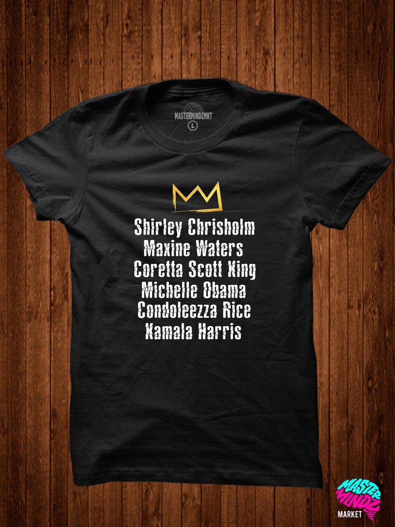 May include: Black t-shirt featuring a gold crown and the names of influential women in white text: Shirley Chrisholm, Maxine Waters, Coretta Scott King, Michelle Obama, Condoleezza Rice, Kamala Harris.