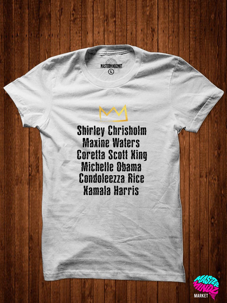 May include: White t-shirt featuring a gold crown and a list of names: Shirley Chrisholm, Maxine Waters, Coretta Scott King, Michelle Obama, Condoleezza Rice, Kamala Harris.