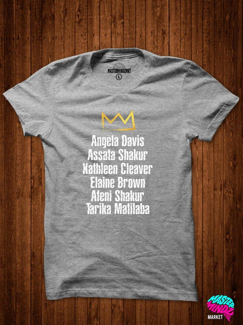 May include: Gray t-shirt with a gold crown and the names Angela Davis, Assata Shakur, Kathleen Cleaver, Elaine Brown, Afeni Shakur, and Tarika Matilaba printed on it.