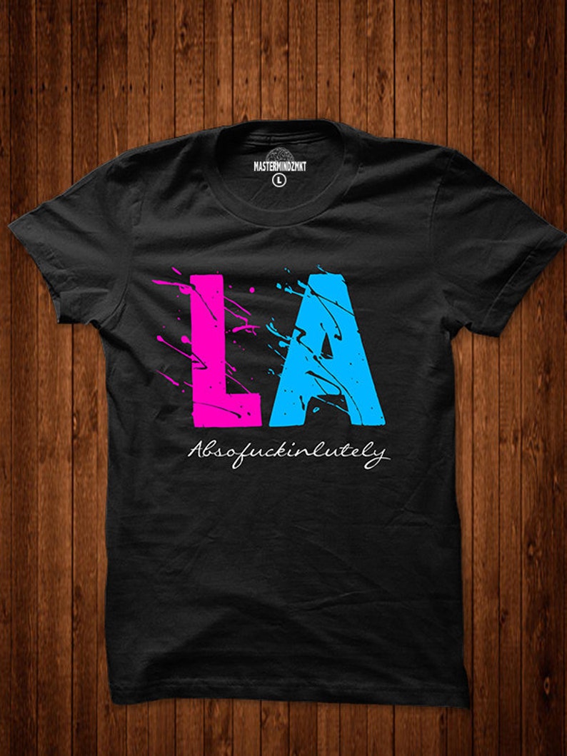 May include: Black t-shirt with a pink and blue paint splatter design that spells out "LA" and the text "Absofuckinlutely" underneath.