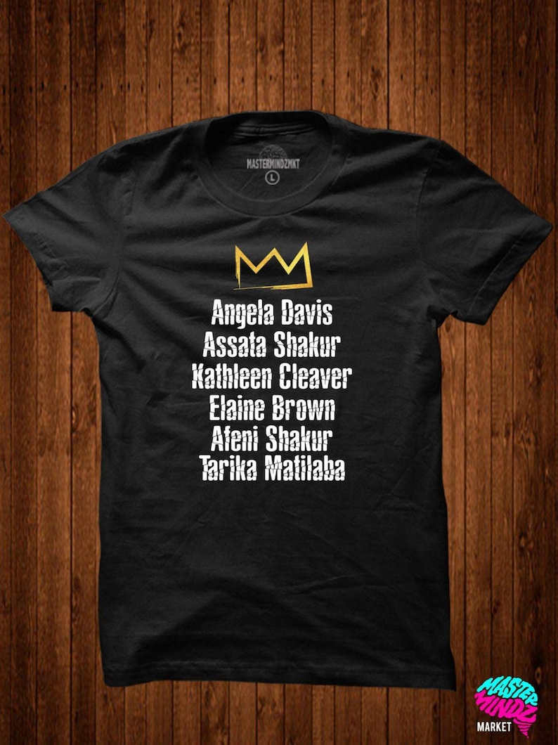 May include: Black t-shirt with a gold crown and the names Angela Davis, Assata Shakur, Kathleen Cleaver, Elaine Brown, Afeni Shakur, and Tarika Matilaba printed in white.