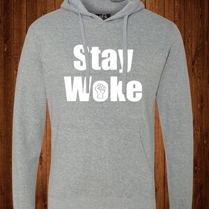 May include: A gray hooded sweatshirt with the text "Stay Woke" in white lettering. A raised fist is included in the text.