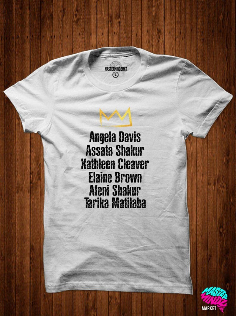 May include: White t-shirt with a gold crown and a list of names: Angela Davis, Assata Shakur, Kathleen Cleaver, Elaine Brown, Afeni Shakur, Tarika Matilaba.