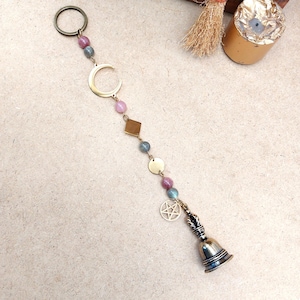 Può includere: Una decorazione a vento con una luna crescente in ottone, forme geometriche e una piccola campana. La decorazione presenta perline rosa e blu, un ciondolo a pentagramma e una finitura in metallo color bronzo.