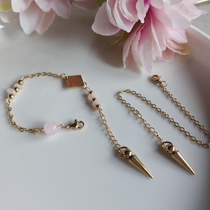 Peut inclure: Un bracelet doré et deux accessoires de chaîne assortis. Le bracelet présente un accent carré, des perles de pierres précieuses roses et une grosse pierre précieuse rose. Les accessoires de chaîne ont des pendentifs dorés en forme de cône.