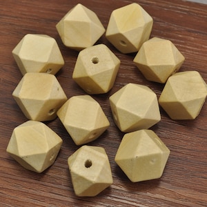 Może przedstawiać: Grupa 12 drewnianych koralików, każdy o geometrycznym, fasetowanym kształcie. Korale są jasnobeżowe i mają otwór przewiercony przez środek.