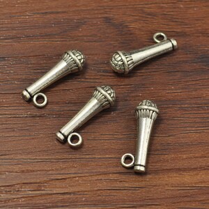 May include: Four silver-toned microphone charms with a loop for attaching to jewelry or other crafts.