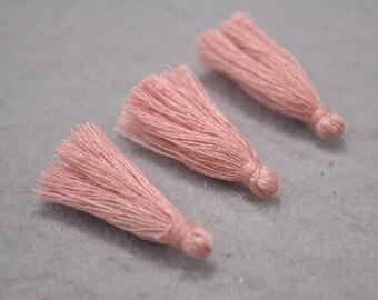 May include: Three pink tassel trims, each with a knotted end. The tassels are made of soft, fluffy yarn and are approximately 2 inches long.